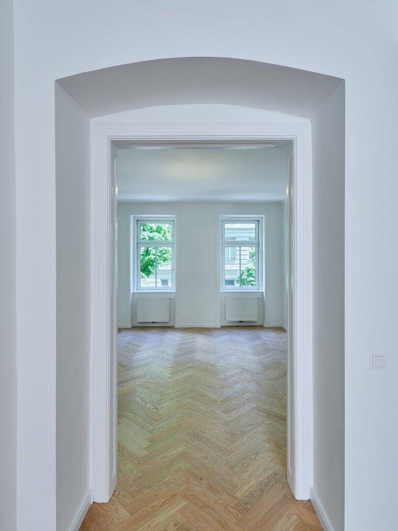 Offener Türbogen im Flur, der den Blick auf zwei helle Fenster in einem angrenzenden Raum freigibt.