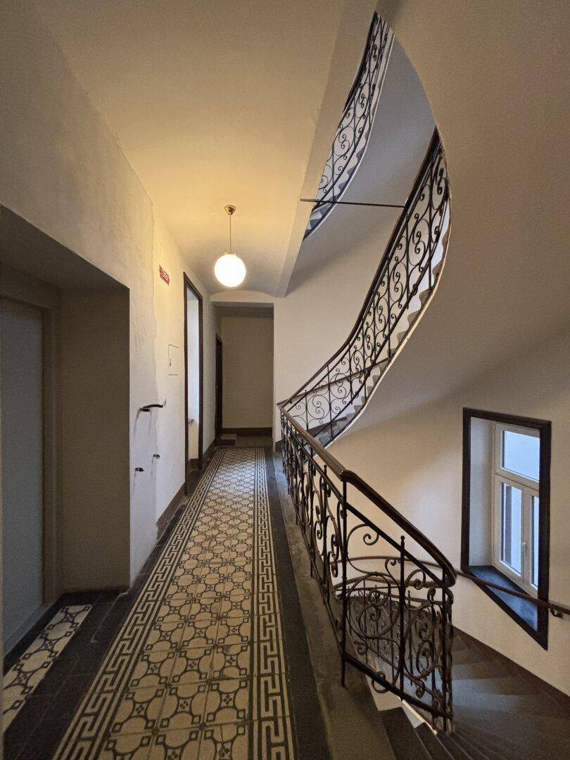 Historisches Treppenhaus mit kunstvollem schmiedeeisernem Geländer und gemustertem Fliesenboden im Altbau.