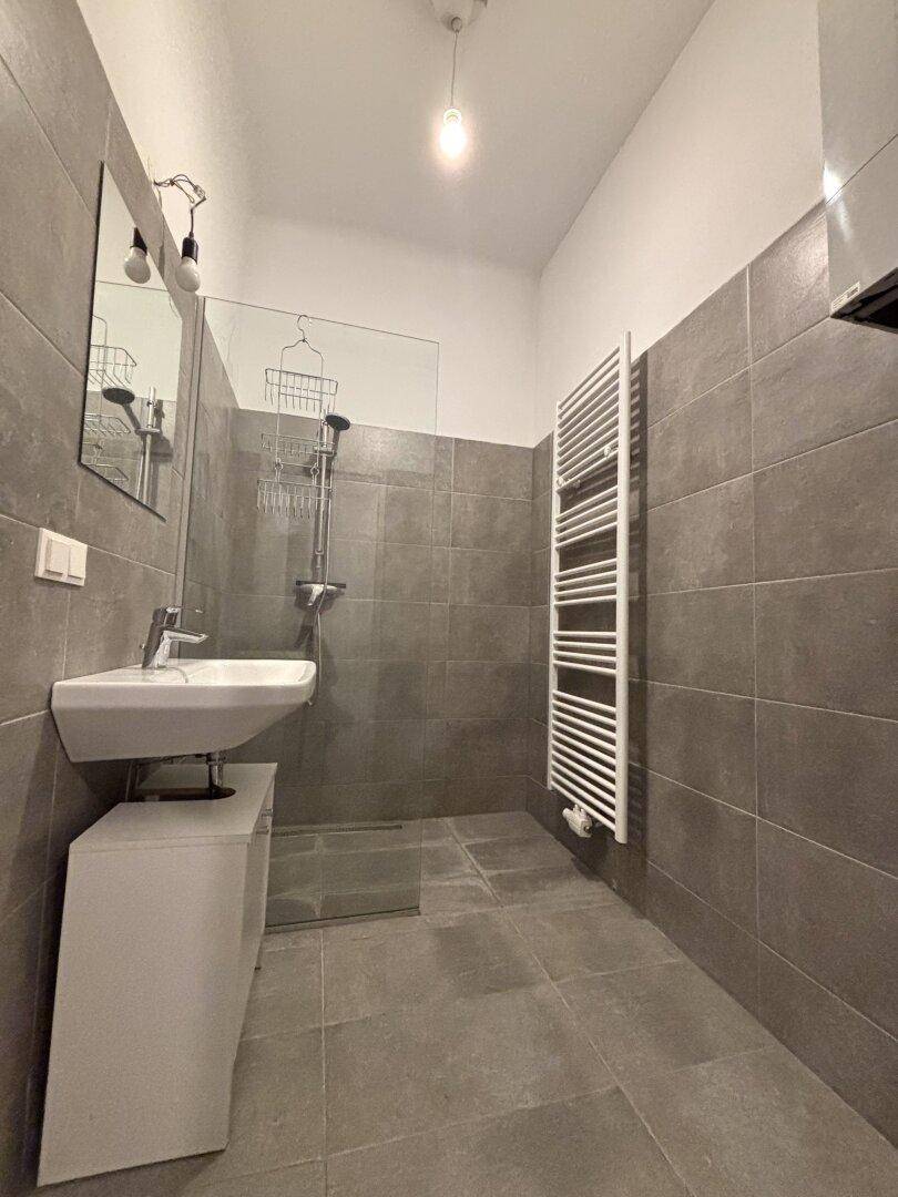 Modernes Badezimmer mit grauen Fliesen, ebenerdiger Dusche und einem praktischen beheizten Handtuchhalter.