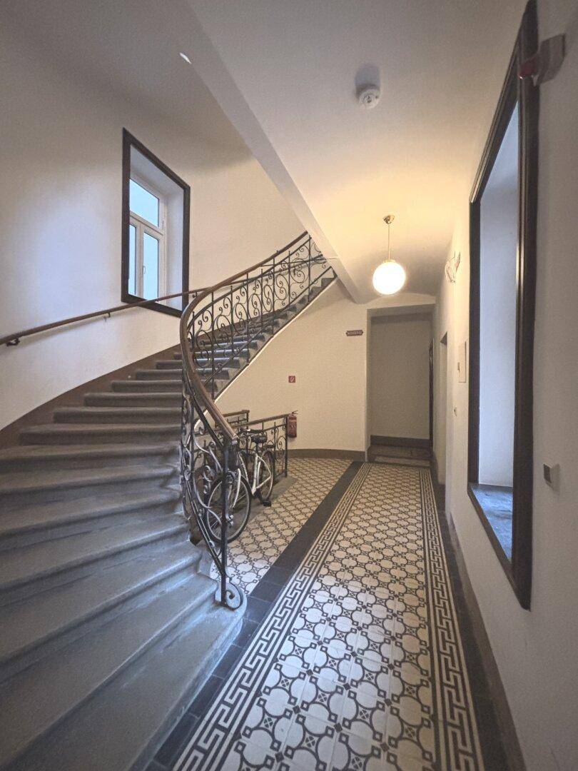Elegantes Treppenhaus mit geschwungenem schmiedeeisernem Geländer und gemusterten Fliesen, das viel Tageslicht erhält.