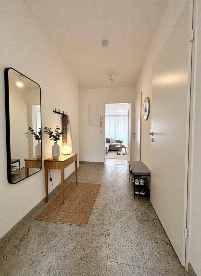 Heller Flur mit Fliesenboden, Spiegel und Garderobe.