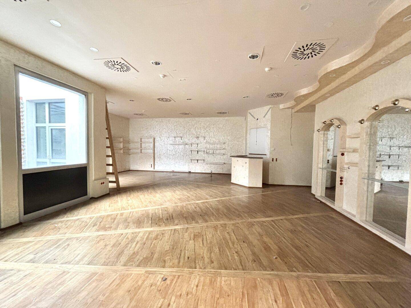 Geräumiger Ladenbereich mit Holzboden, großen Fenstern und dekorativen Wandelementen, bereit zur Einrichtung.
