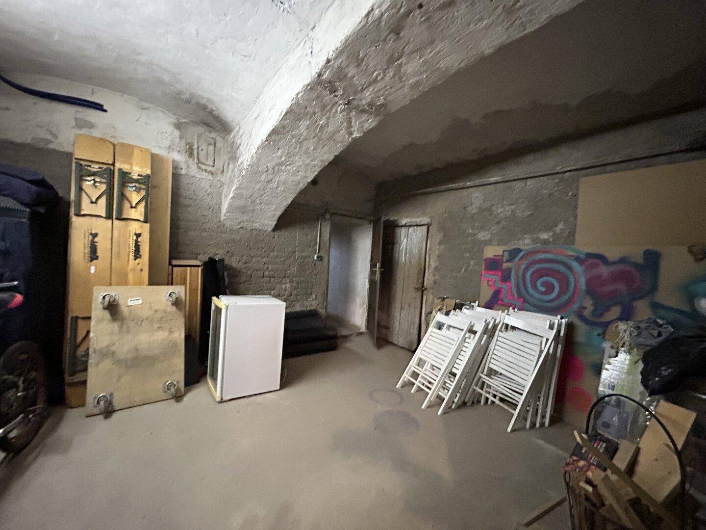 Geräumiger Kellerbereich mit Betonboden, Steinwänden und einem kleinen Kühlschrank, ideal als Lagerraum.