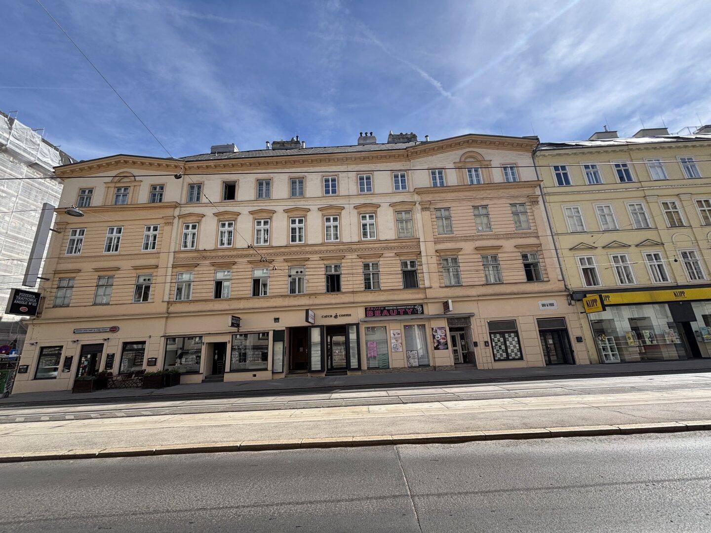 Historisches Mehrfamilienhaus mit klassischer Fassade und Geschäften im Erdgeschoss.