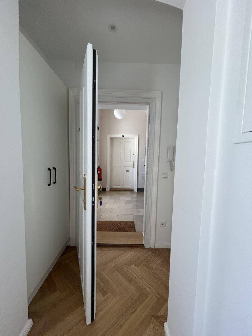 Heller Flur mit Fischgrätparkett und weißen Wänden, der den Blick in weitere Räume freigibt.