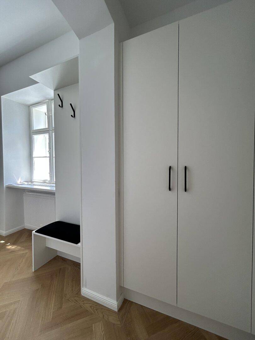 Heller Flur mit Einbauschrank, Sitzbank und Fischgrätparkett.