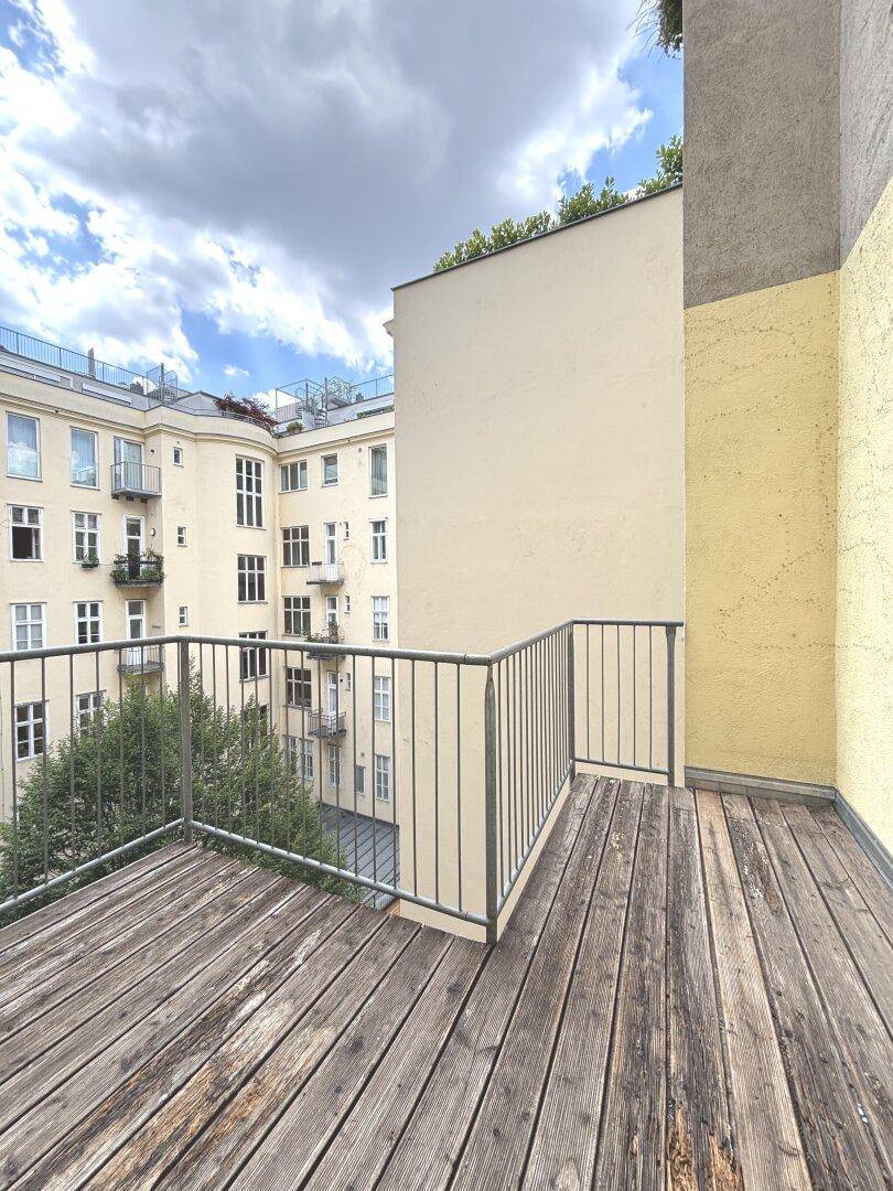Balkon mit Holzdielen und Metallgeländer, bietet einen ruhigen Blick auf den Innenhof.