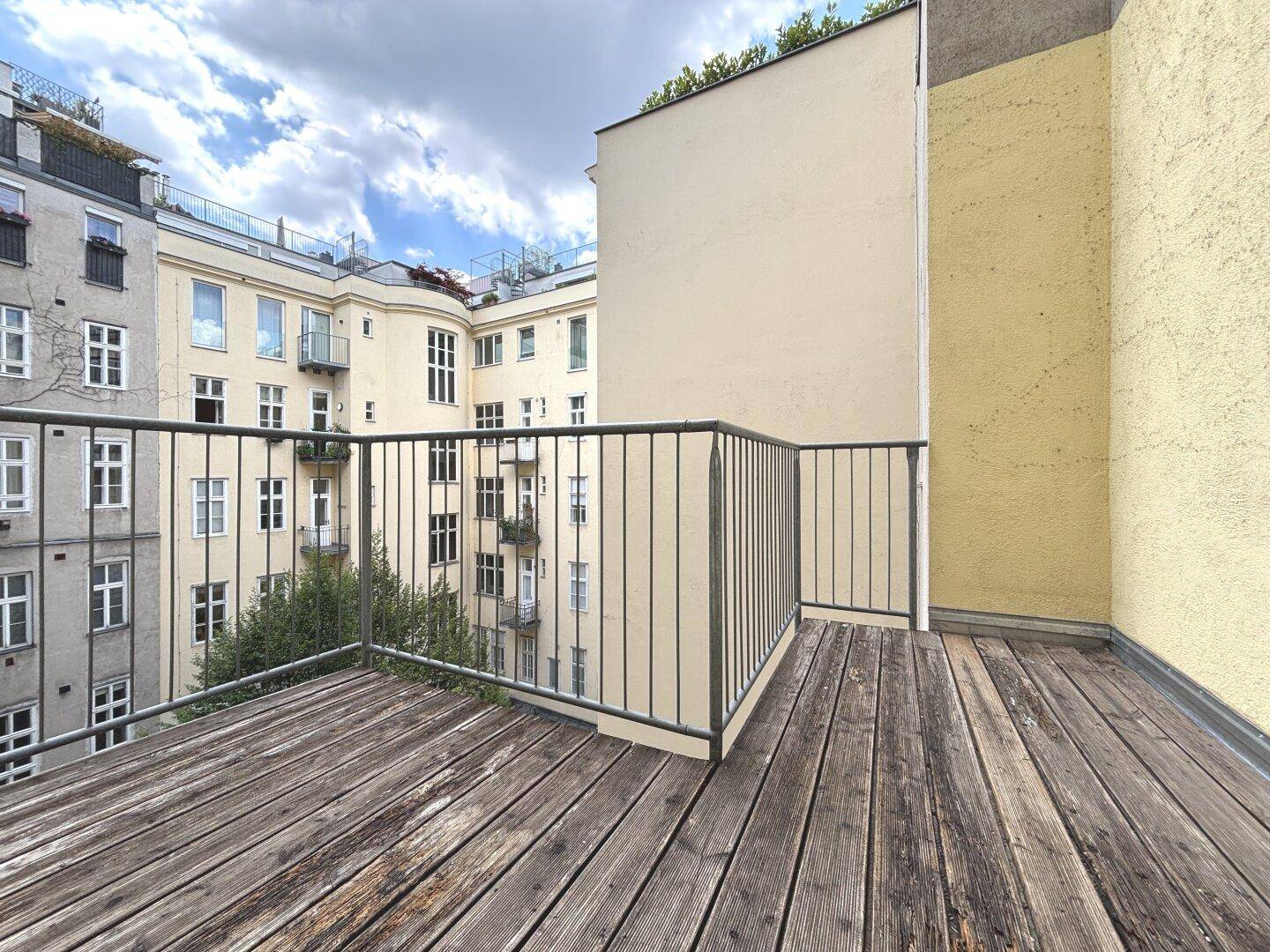 Geräumiger Balkon mit Holzdielen und Metallgeländer, bietet einen ruhigen Blick auf den Innenhof.