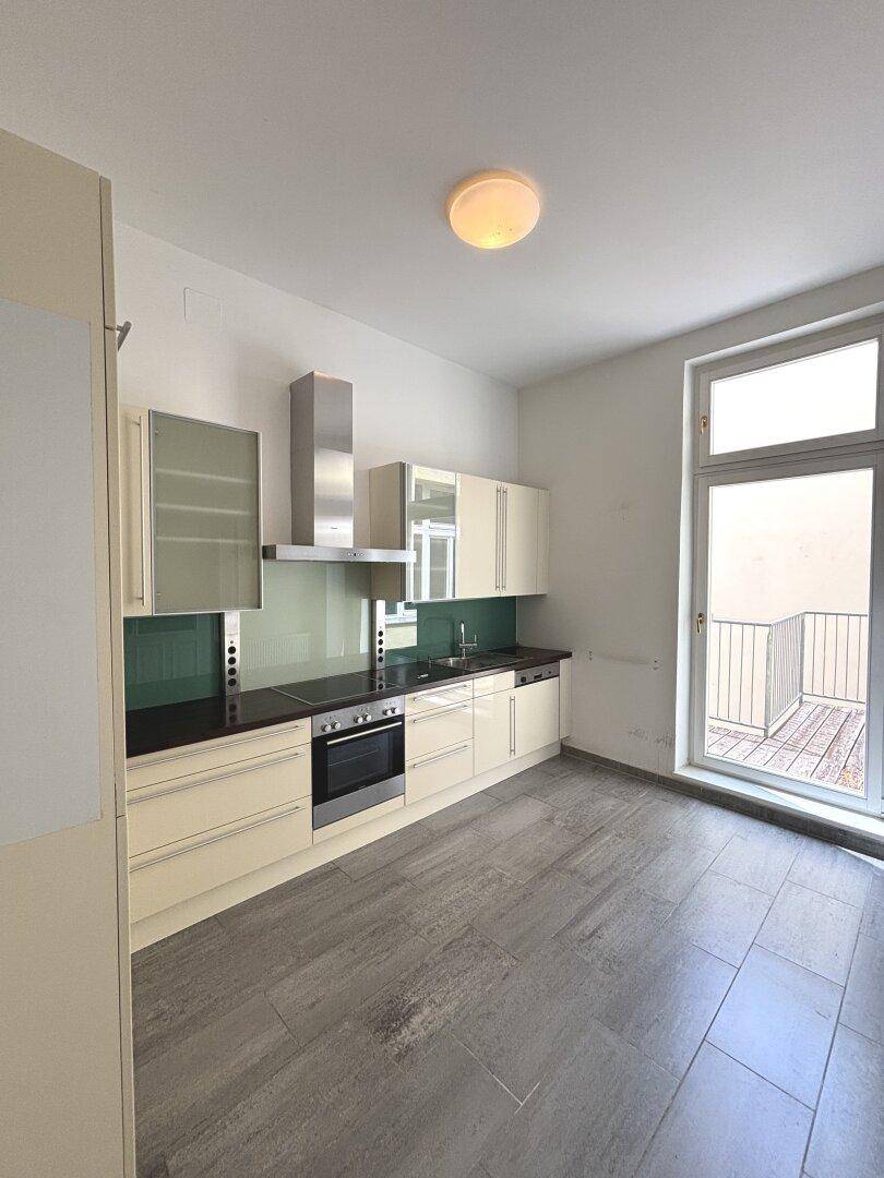 Moderne Einbauküche mit hellen Schränken, dunkler Arbeitsplatte und Zugang zu einem kleinen Balkon.