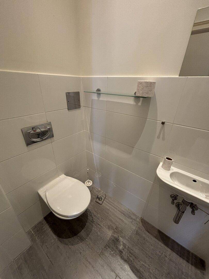 Kleines Gäste-WC mit wandhängendem WC und Handwaschbecken, modern gefliest.