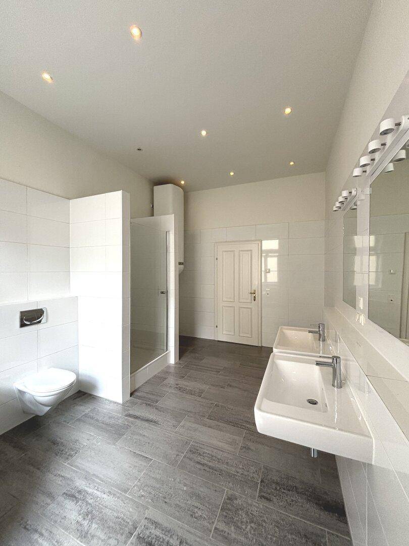 Helles Badezimmer mit Doppelwaschbecken, wandhängendem WC und moderner Duschkabine.