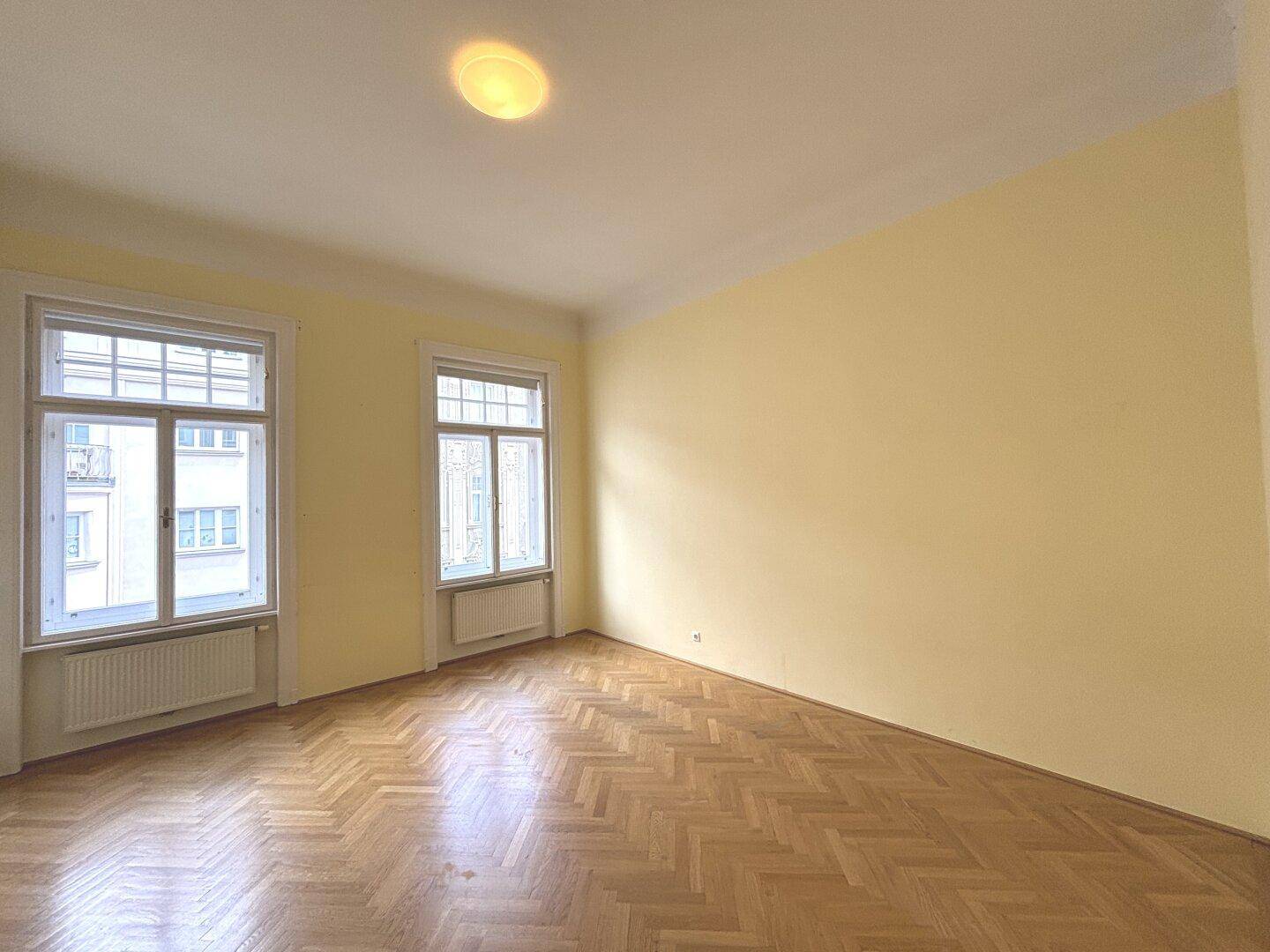Helles Zimmer mit Fischgrätparkett und zwei Fenstern, ideal als Schlaf- oder Kinderzimmer.