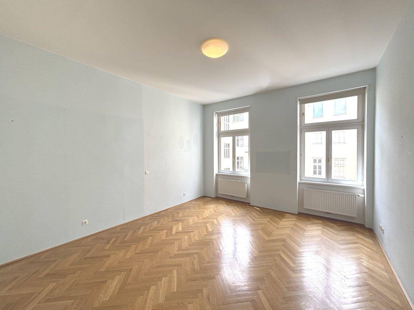 Helles Zimmer mit Fischgrätparkett und zwei großen Fenstern, ideal als Schlaf- oder Arbeitszimmer.