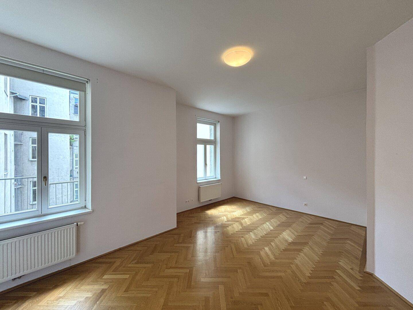 Helles Zimmer mit Fischgrätparkett und zwei Fenstern, ideal für Schlaf- oder Arbeitsbereich.