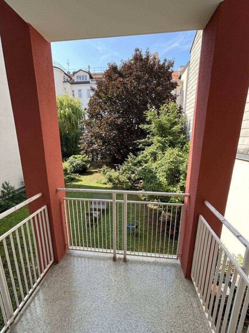Balkon mit weißem Geländer und Blick auf den grünen Innenhof.
