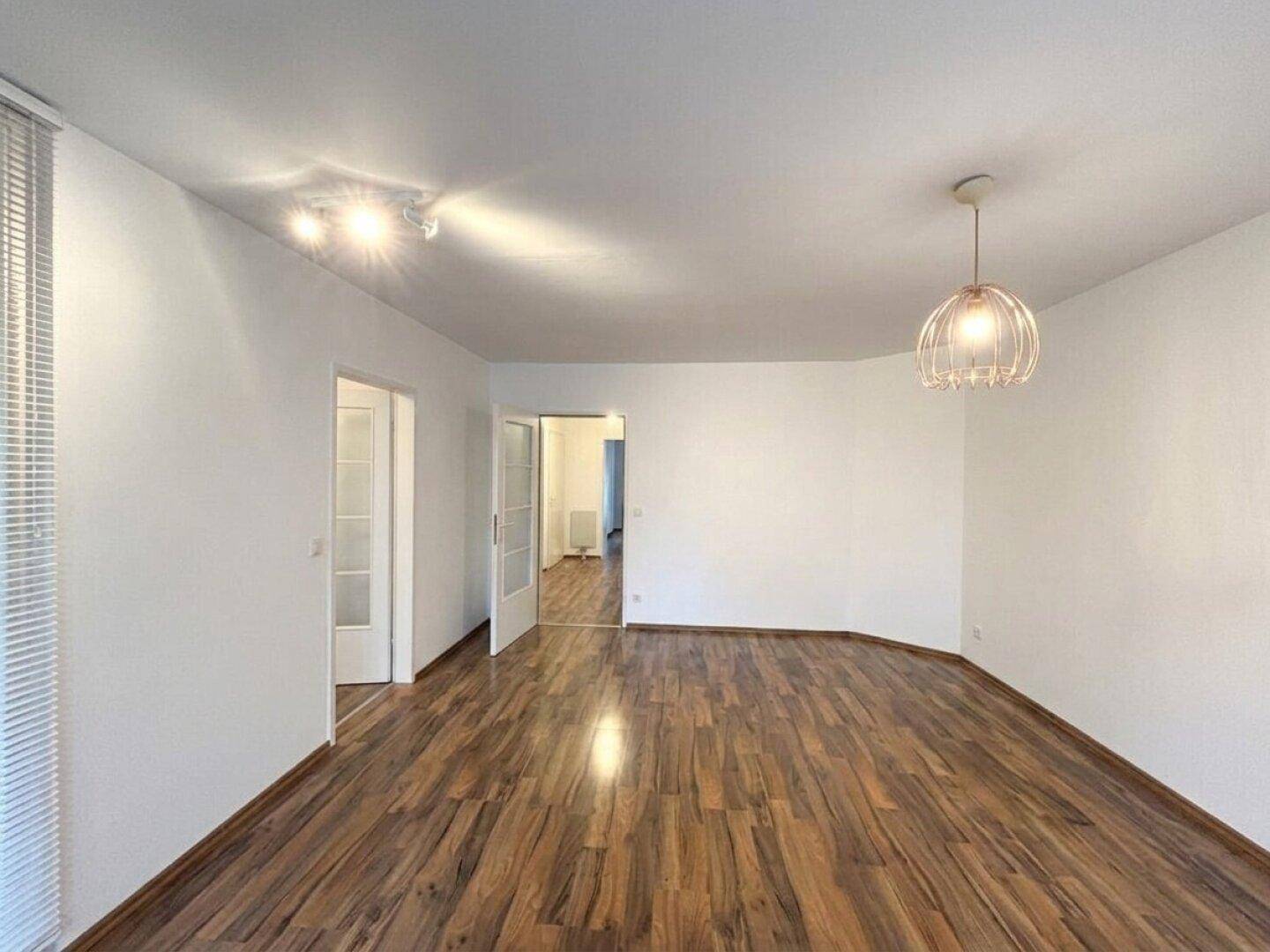Heller Wohnbereich mit Holzboden und Durchgang zu weiteren Räumen.