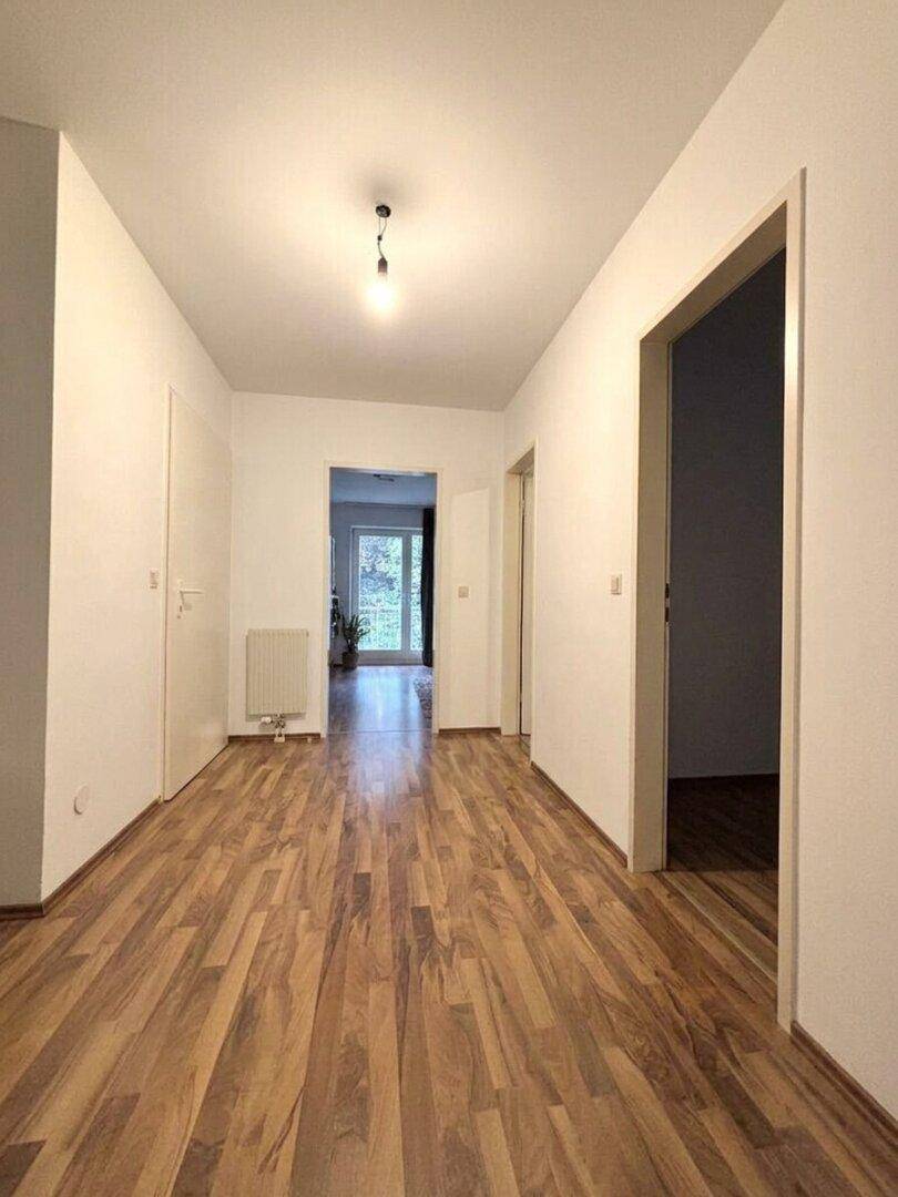 Langer Flur mit Holzboden, weißen Wänden und Blick in den hinteren Bereich.