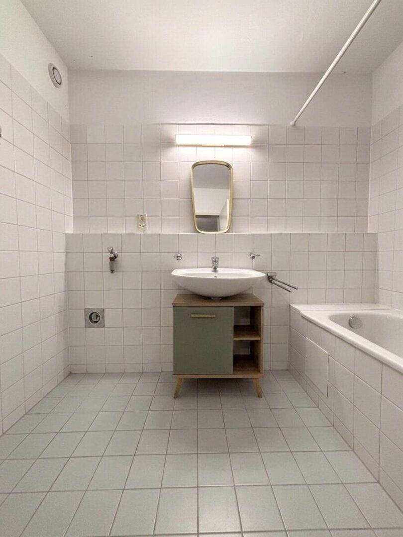 Helles Badezimmer mit weißen Fliesen, Waschbecken und Badewanne.