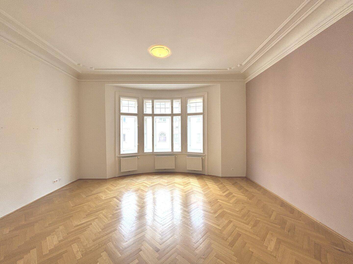 Geräumiges Zimmer mit Fischgrätparkett, Erkerfenster und hohen Decken, bereit zur individuellen Gestaltung.