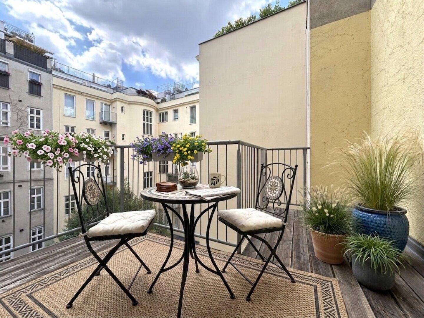 Gemütlicher Balkon mit Holzboden, schmiedeeisernen Möbeln und Blumenkästen mit Blick auf den Innenhof.