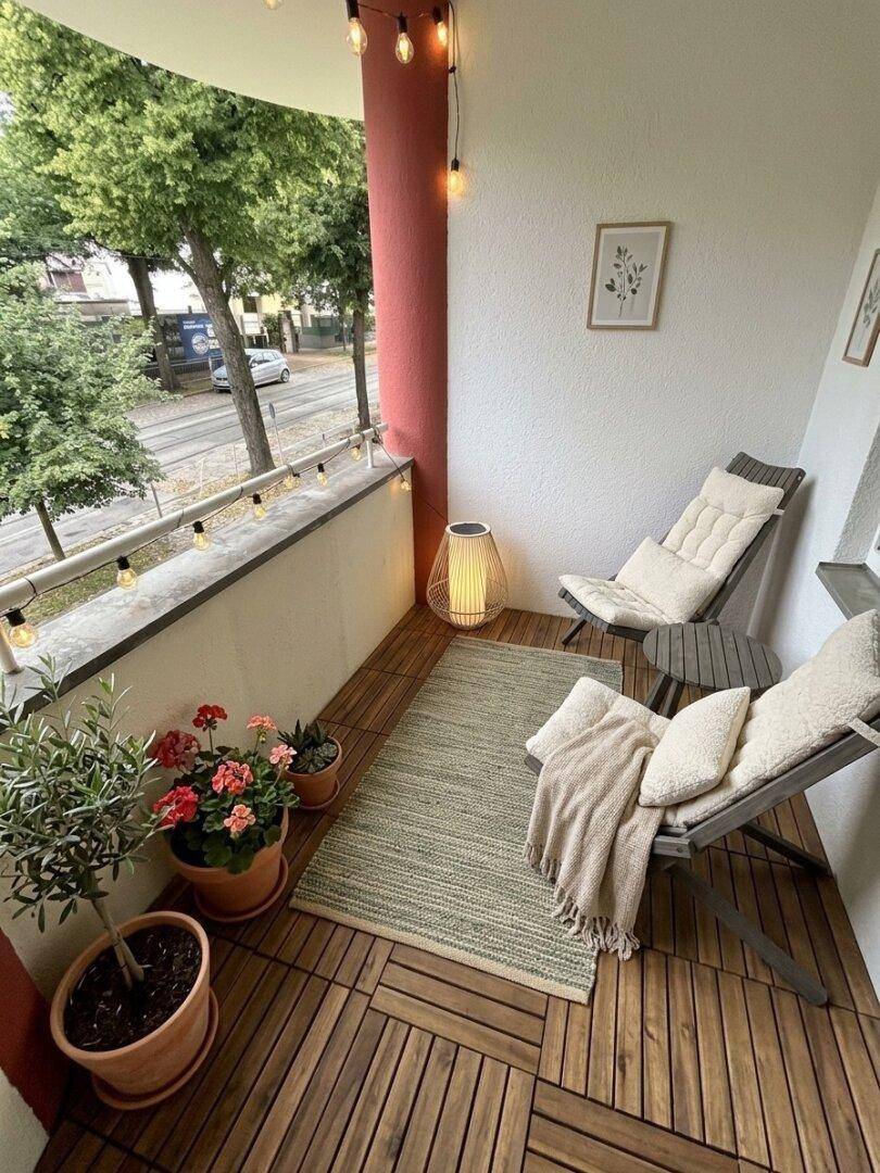 Kleiner Balkon mit Holzbodenfliesen, Lichterkette und Blick auf die Straße.