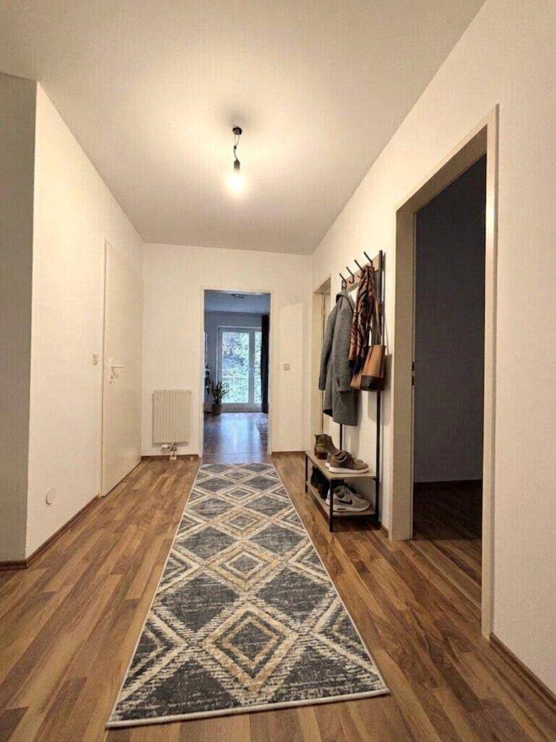 Heller Flur mit Holzboden, Garderobe und einem langen Teppich.