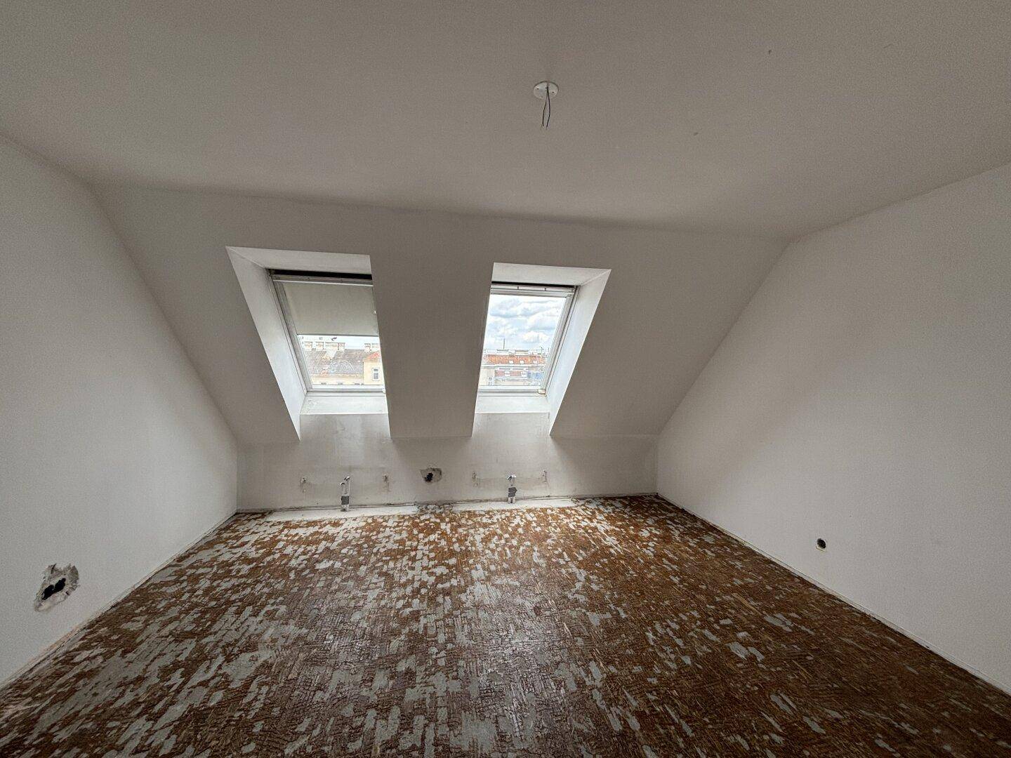 Unfertiger Raum im Dachgeschoss mit schrägen Wänden und zwei Dachfenstern, bereit für den Ausbau.