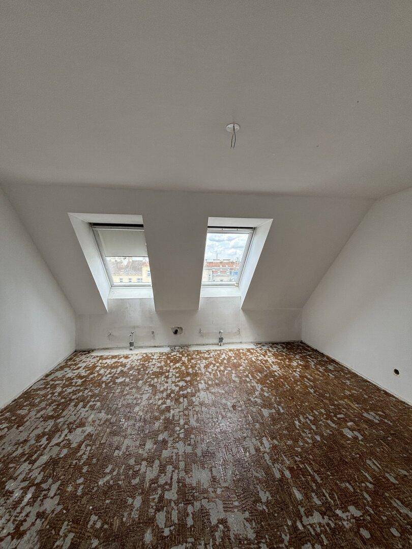 Dachgeschossraum mit schrägen Wänden und zwei Dachfenstern, der auf den Innenausbau wartet.