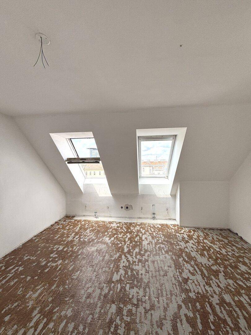 Heller Dachgeschossraum mit zwei Dachfenstern und schrägen Wänden, ideal für einen individuellen Ausbau.