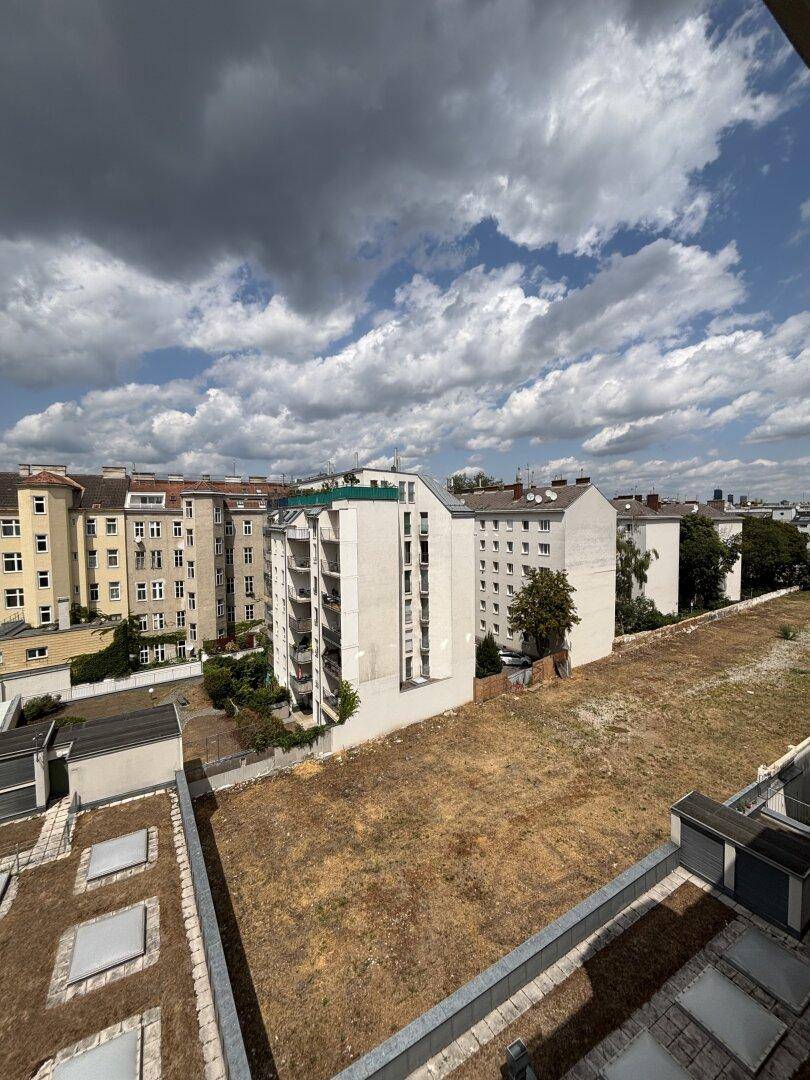 Weitläufiger Blick über städtische Gebäude und eine große unbebaute Fläche unter bewölktem Himmel.