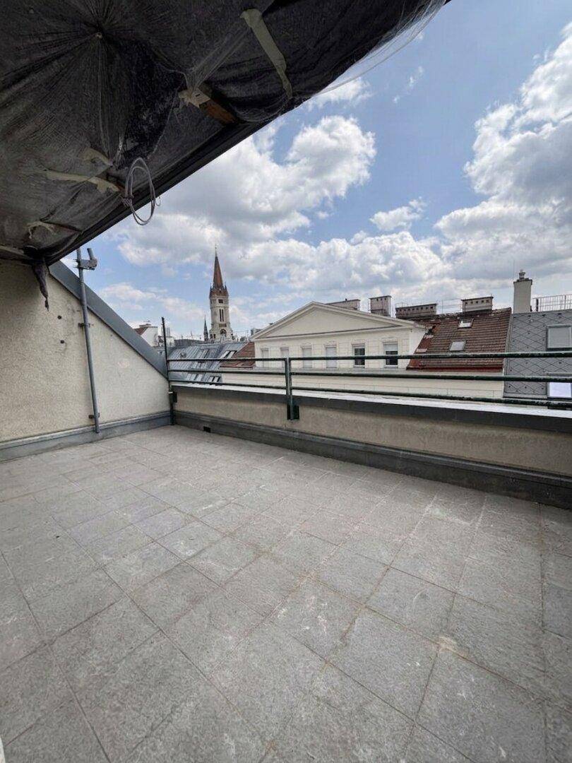 Unmöblierter Balkon mit Fliesenboden und Blick auf die Dächer der Stadt und einen Kirchturm.