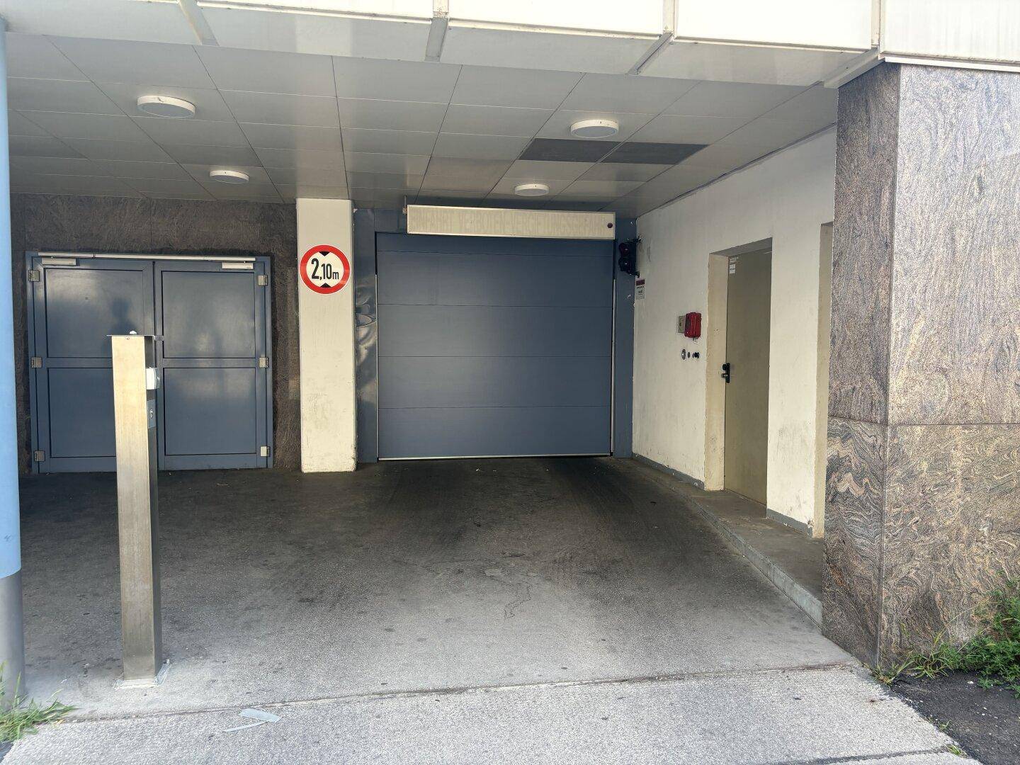 Einfahrt zu einer Tiefgarage mit Höhenbegrenzung und Zugangstüren zum Gebäude.