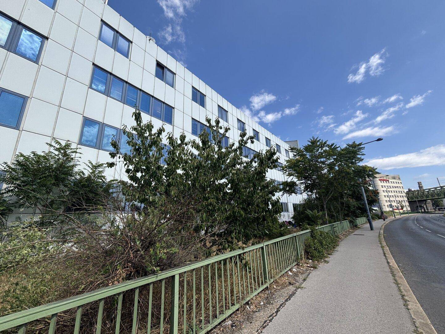 Moderne Bürogebäude-Fassade mit vielen Fenstern und umgebender Vegetation unter blauem Himmel.