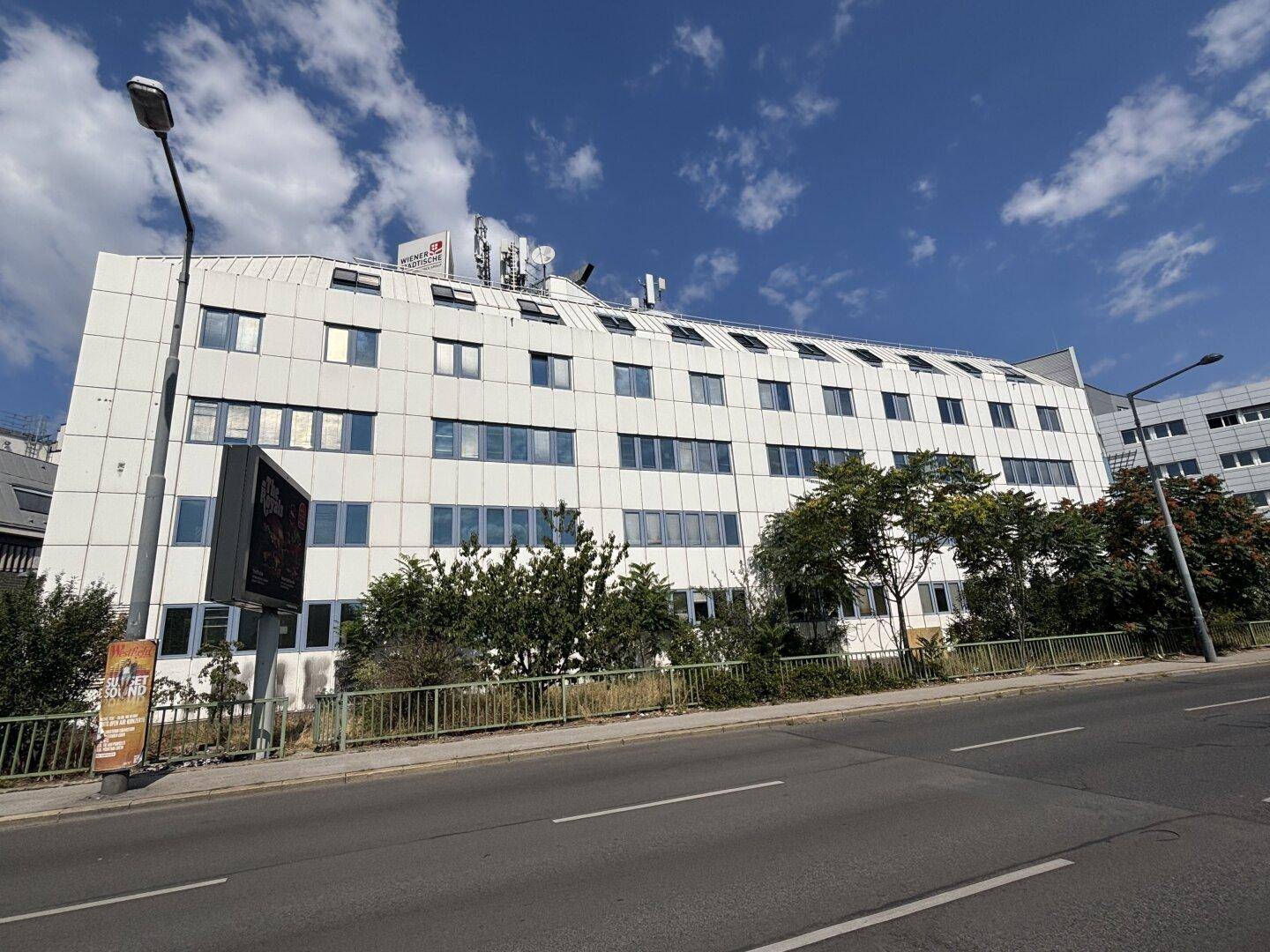 Modernes Bürogebäude mit weißer Fassade und blauen Fenstern an einer belebten Straße.