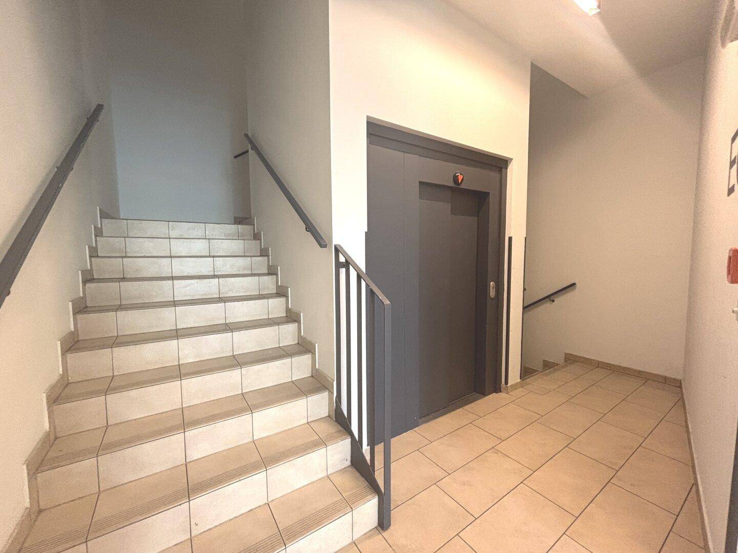 Treppenhaus mit Aufzug und Fliesenboden, verbindet die verschiedenen Etagen des Gebäudes.