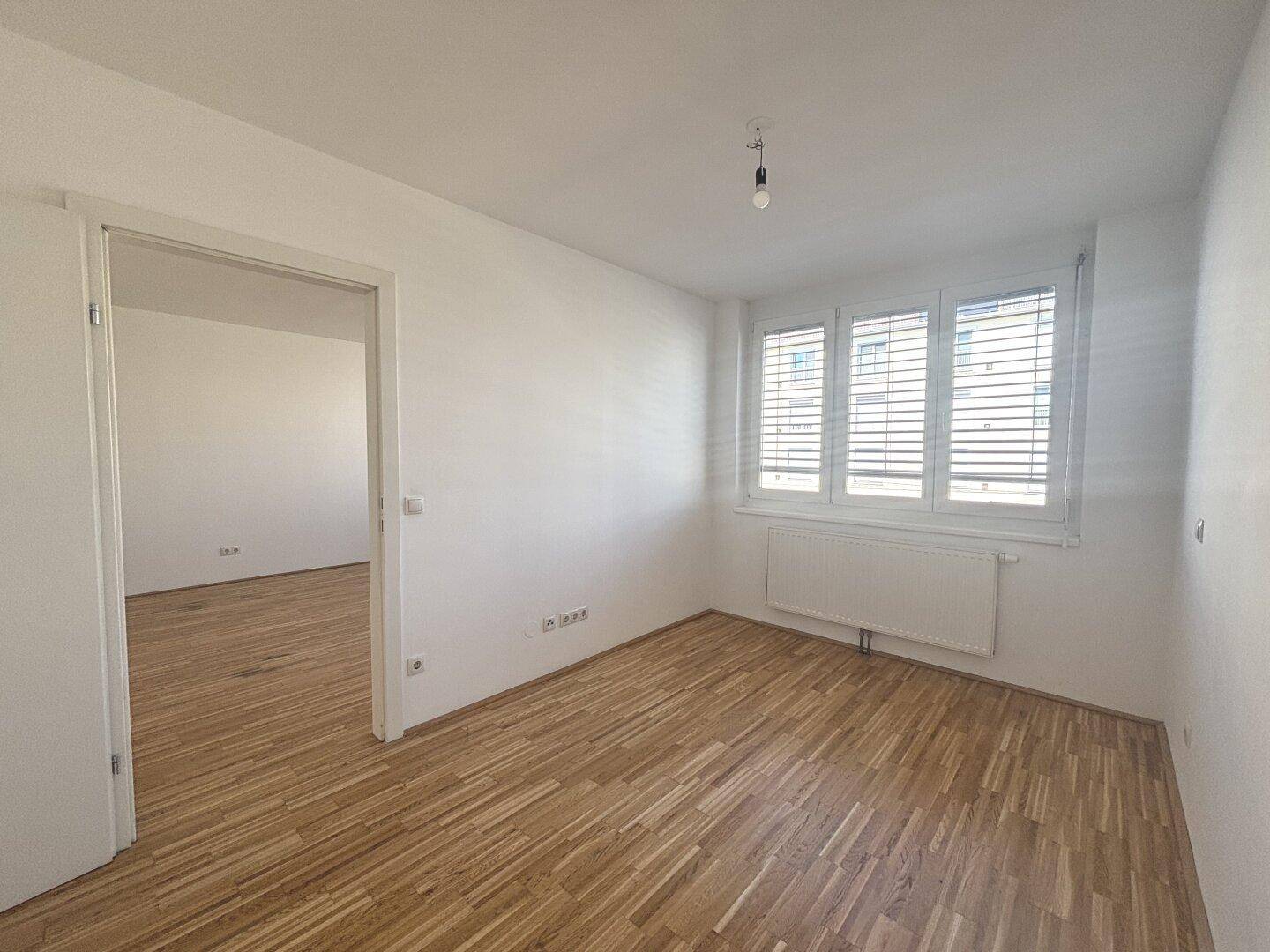 Helles, leeres Zimmer mit Parkettboden und Fenster, ideal als Schlaf- oder Arbeitszimmer.