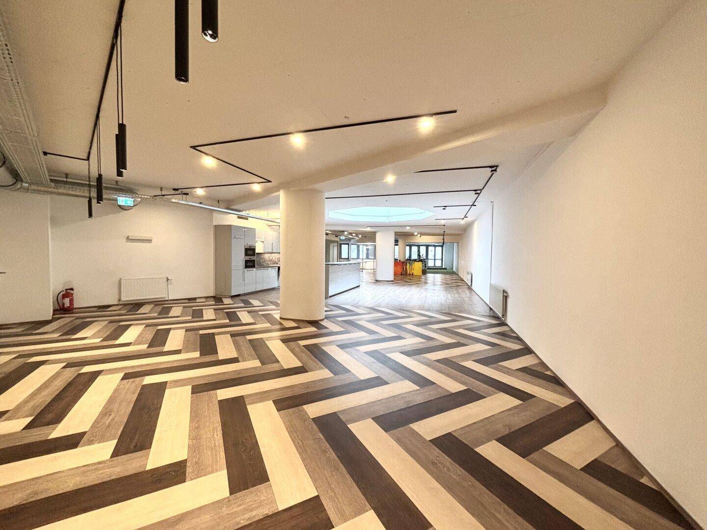 Weitläufiger, offener Bürobereich mit markantem Fischgrätboden, Säule und moderner Beleuchtung.