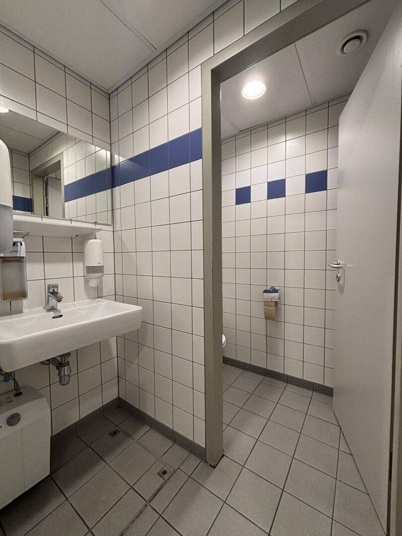 Gefliestes Badezimmer mit Waschbecken, Spiegel und blauen Akzentstreifen an den Wänden.