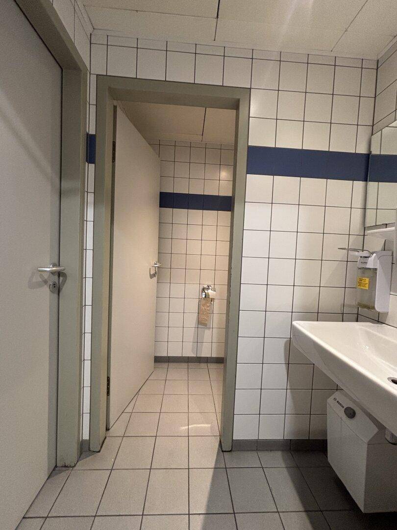 Gefliestes Badezimmer mit Waschbecken und Zugang zu einer Toilette, gekennzeichnet durch blaue Akzente.