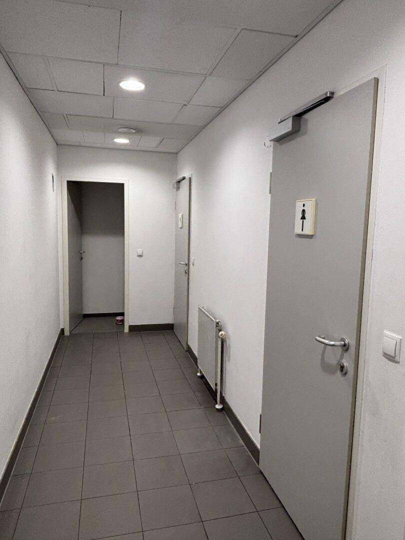 Langer Flur mit grauen Fliesen, weißen Wänden und mehreren Türen, die zu verschiedenen Räumen führen.