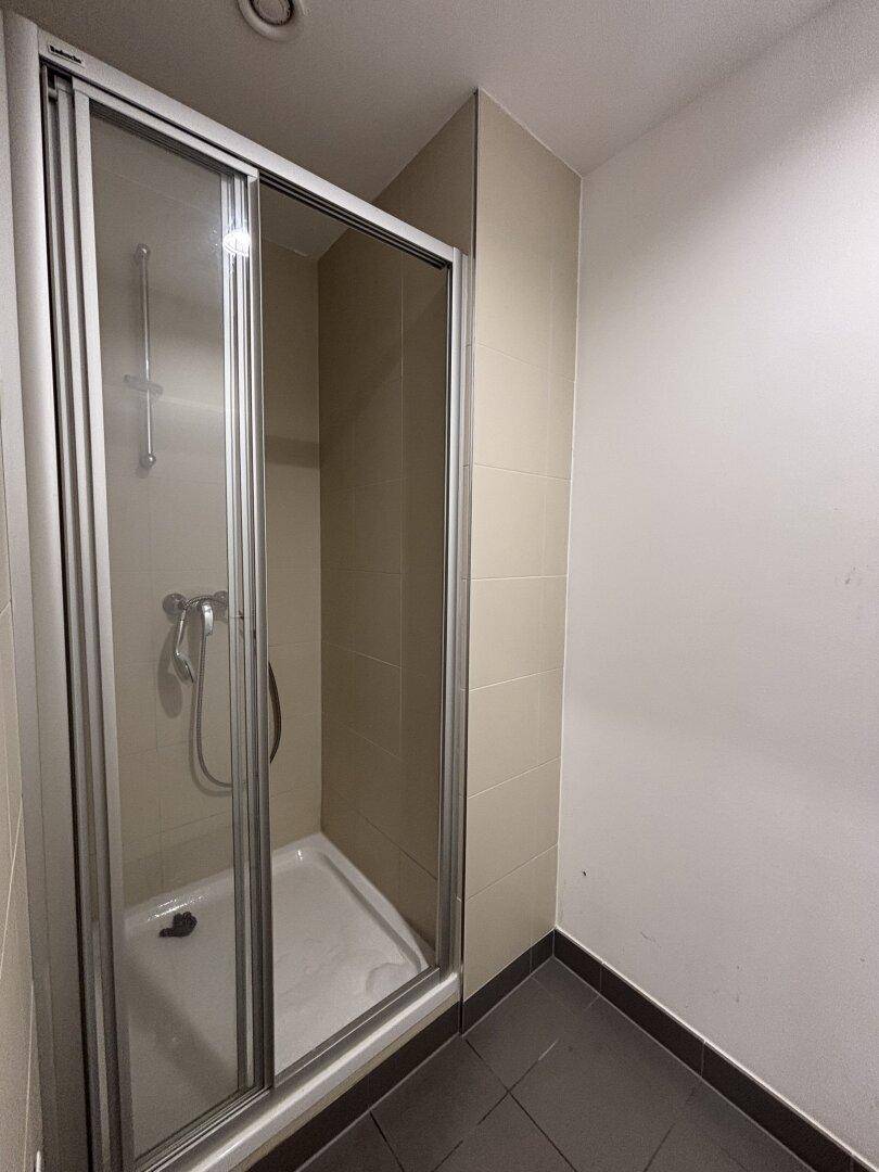 Duschkabine mit Glasschiebetür in einem gefliesten Badezimmer mit beigen Wandfliesen.