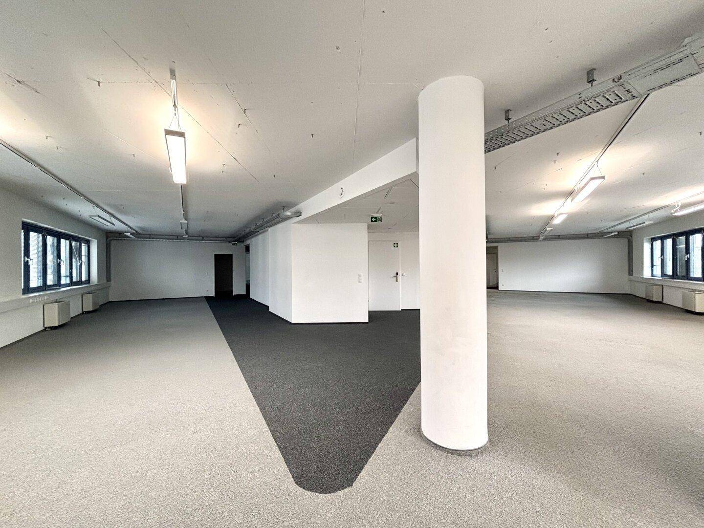 Großer, offener Büroraum mit Säule, Teppichboden und Fenstern, ideal für flexible Arbeitsplatzgestaltung.