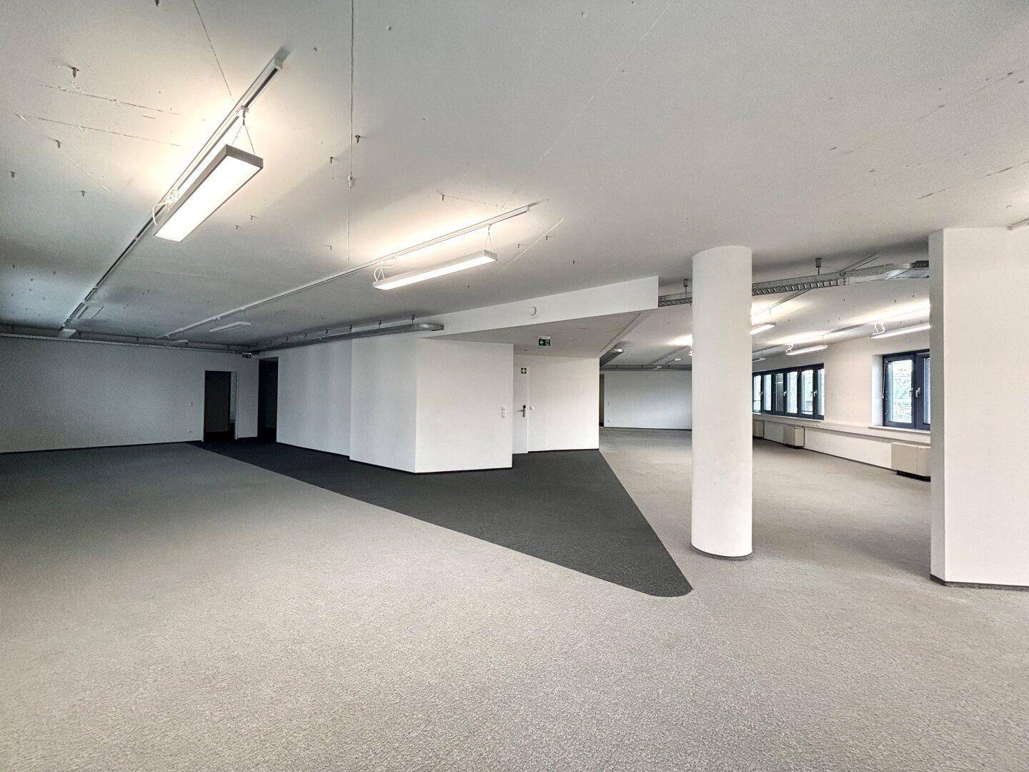 Großer, offener Büroraum mit Säule, Teppichboden und Fenstern, ideal für flexible Arbeitsplatzgestaltung.