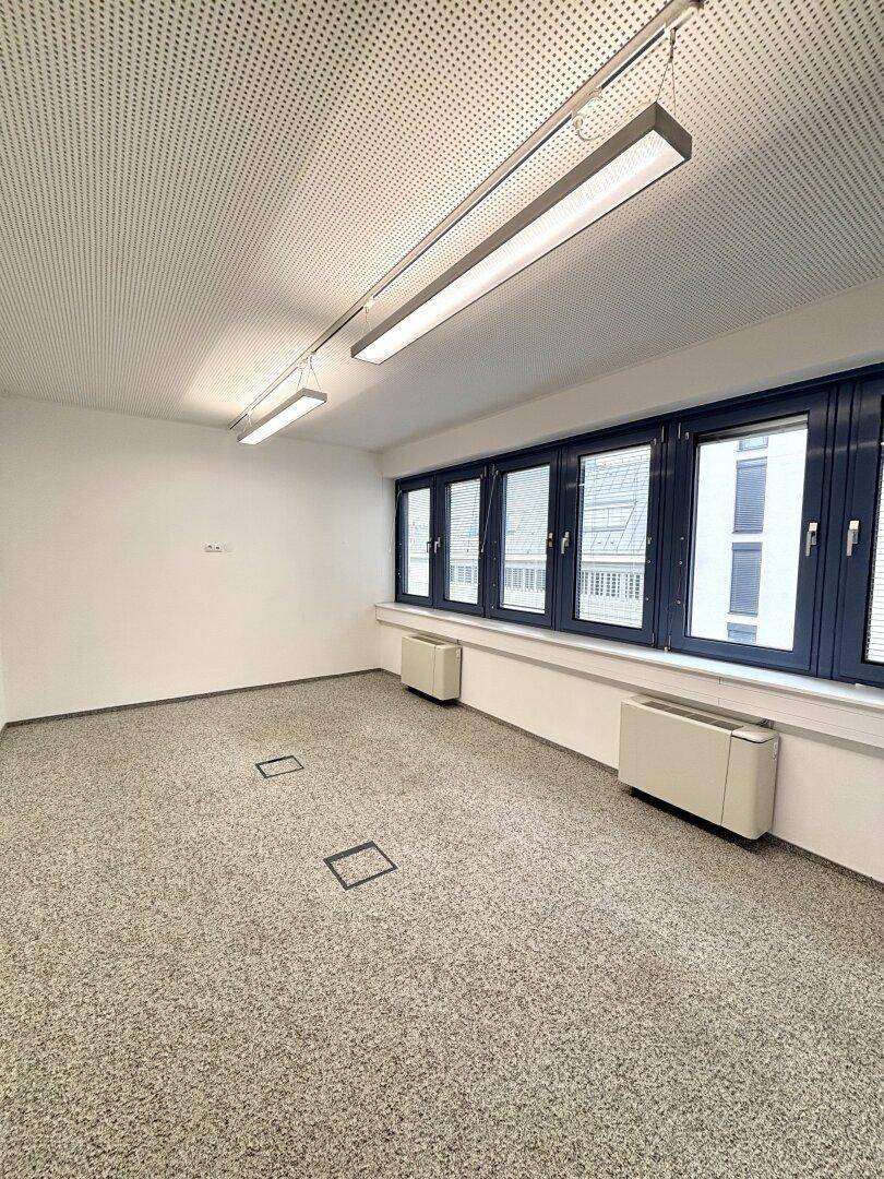 Kleiner Büroraum mit Teppichboden, Fenstern und Bodentanks für Strom und Daten.