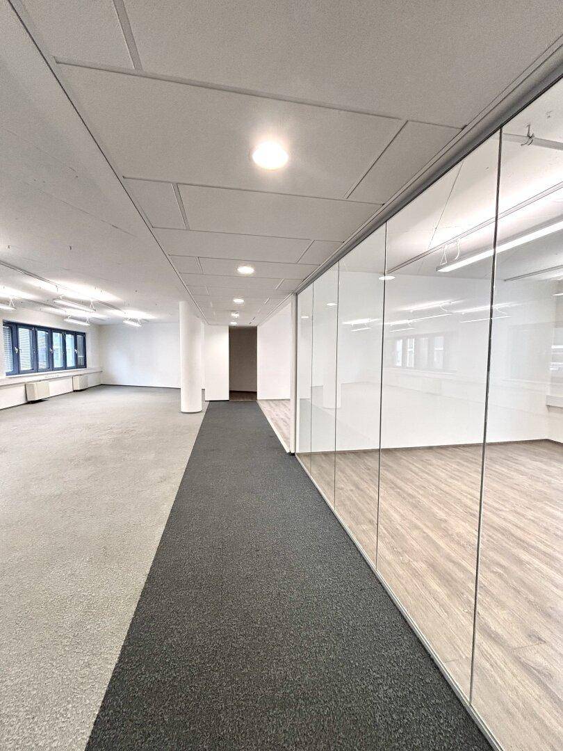 Moderner Bürogang mit Teppichboden und Glaswänden, die separate Büros abgrenzen.