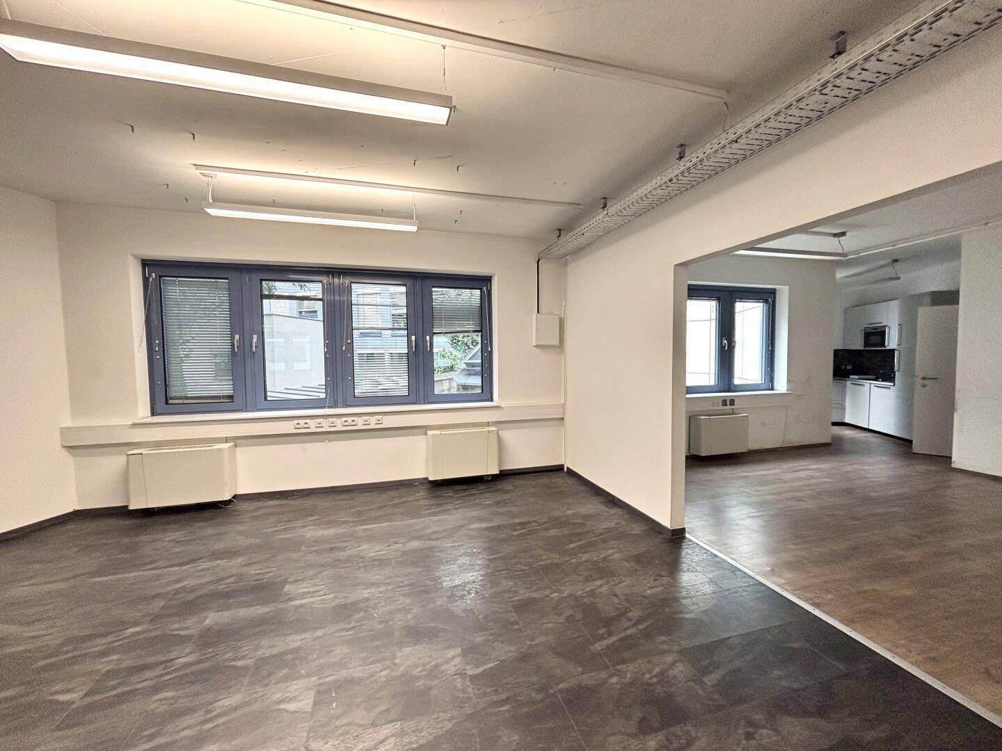 Bürobereich mit dunklem Fliesenboden und angrenzender Küchenzeile, die durch einen Durchgang verbunden ist.