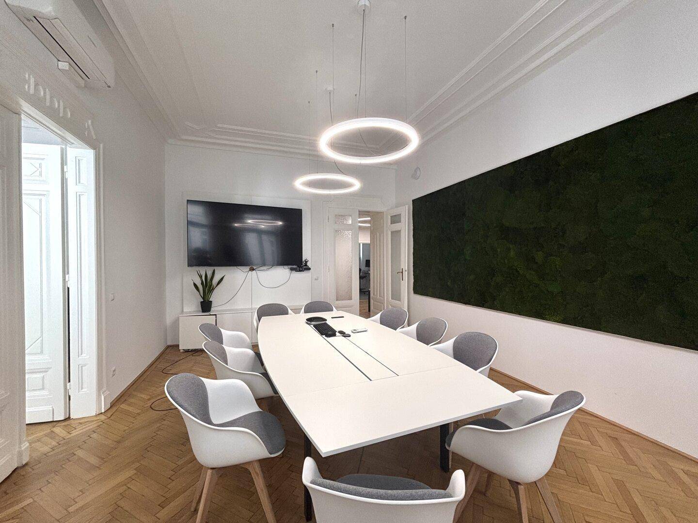 Moderner Konferenzraum mit Fischgrätparkett, ovaler Tafel, ergonomischen Stühlen und einer Mooswand.
