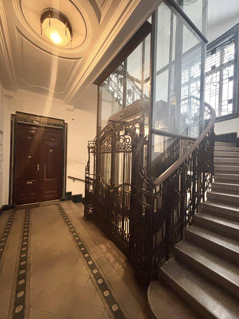 Historischer Eingangsbereich mit kunstvollem Treppenhaus, Aufzug und verzierten Details.