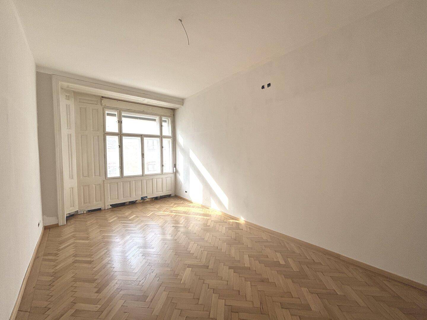 Heller Raum mit Fischgrätparkett und großen Fenstern, bereit für die individuelle Gestaltung.