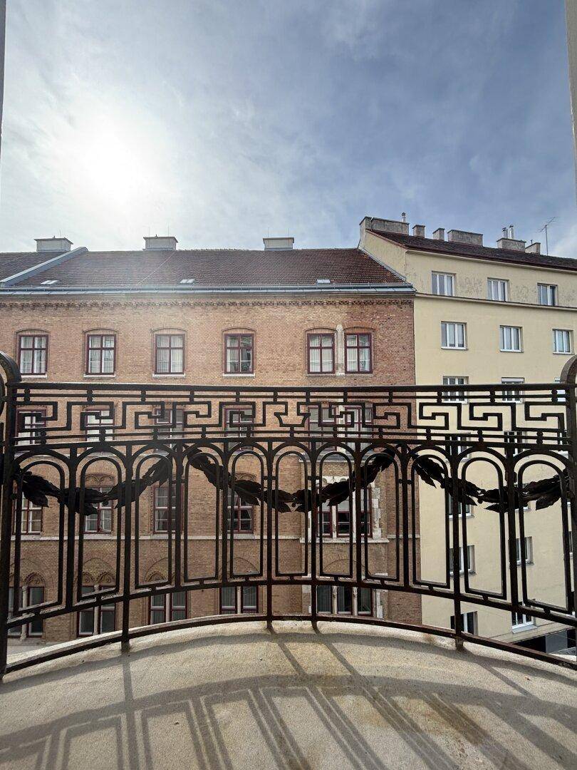Blick vom Balkon auf die gegenüberliegenden Gebäude unter blauem Himmel, mit kunstvollem Geländer.